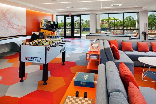 A modern lounge area featuring a foosball table, arcade games, and comfortable seating with colorful flooring.