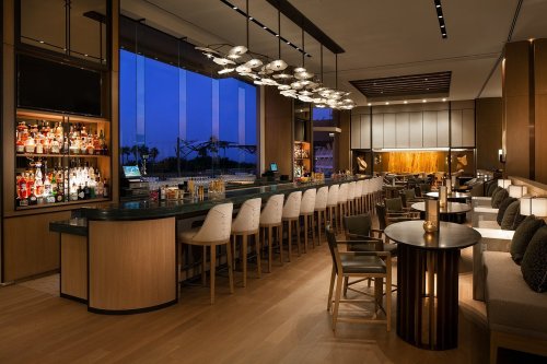 A modern bar with a sleek design, featuring a long counter, stylish seating, and a variety of illuminated bottles.