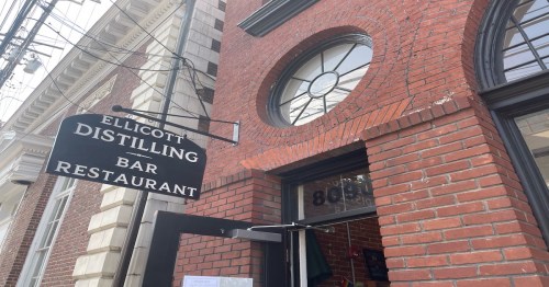 Sign for Ellicott Distilling Bar Restaurant on a brick building, featuring a round window above the entrance.