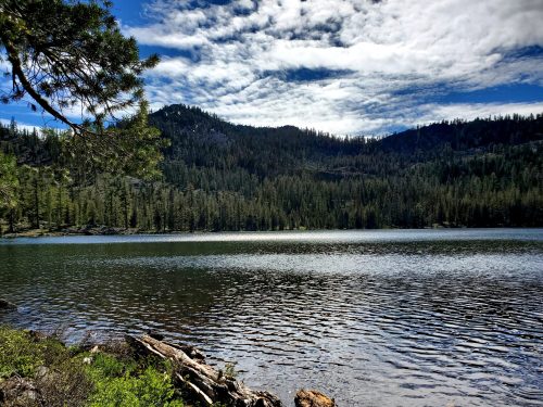 A serene lake surrounded by lush forests and mountains under a partly cloudy sky.