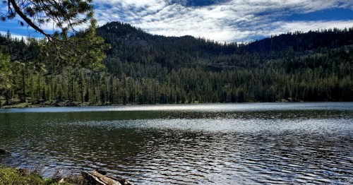 A serene lake surrounded by lush green forests and mountains under a partly cloudy sky.