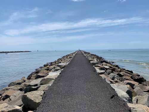 A long stone jetty extends into calm waters under a clear blue sky, with gentle waves lapping at the sides.