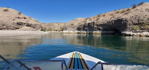 View from the front of a boat on calm water, surrounded by rocky cliffs and clear blue skies.