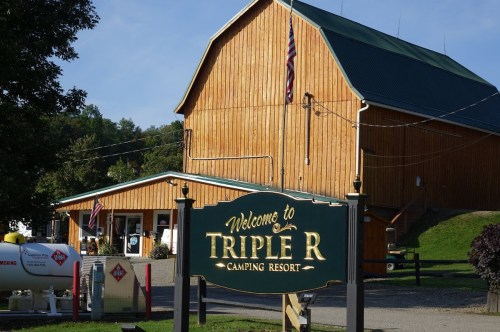 A wooden building with a green sign reading "Welcome to Triple R Camping Resort" in front, surrounded by trees.