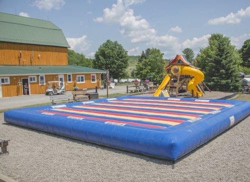 A colorful inflatable bounce pad in a playground area with a slide and a wooden building in the background.