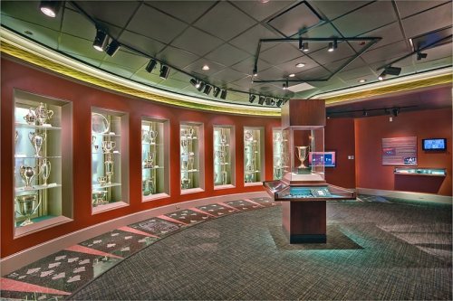 A modern trophy room featuring glass display cases filled with various trophies and awards, illuminated by overhead lights.