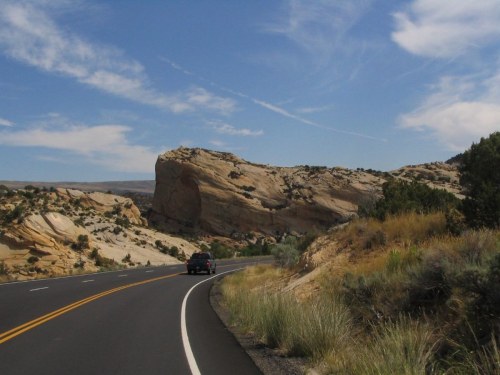 A winding road curves around a rocky landscape under a blue sky with wispy clouds.