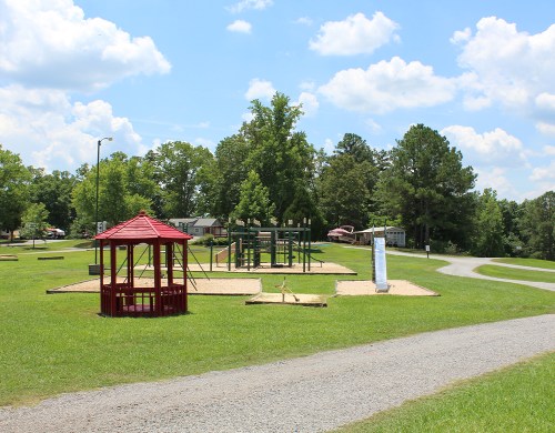 A playground with a red gazebo, climbing structure, and grassy area under a blue sky with fluffy clouds.