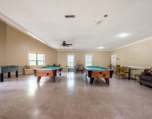 A spacious game room featuring two pool tables, a foosball table, and seating areas with natural light.