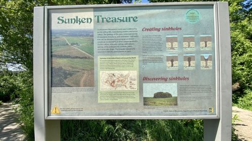 Informational sign about sinkholes, featuring maps and illustrations, set in a natural landscape.