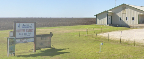 A rural market sign in front of a building, surrounded by open fields and a clear blue sky.