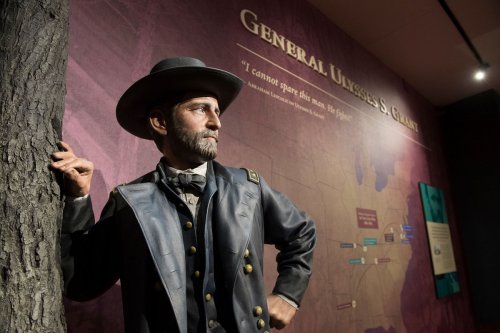 A lifelike statue of General Ulysses S. Grant stands beside a tree, with a historical map and quote in the background.