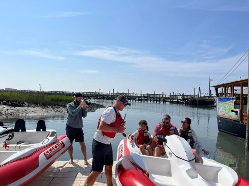 A group of people on a dock near boats, preparing for a day on the water with a scenic view in the background.