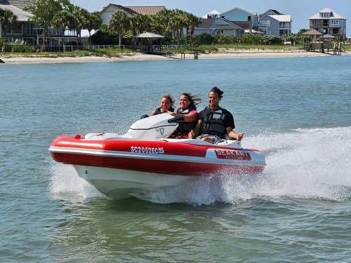Three people enjoy a thrilling ride on a red and white jet ski, speeding across a calm blue waterway.