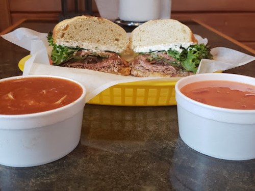 A sandwich with layers of meat and lettuce, served with two bowls of soup on a yellow plate.