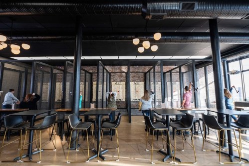 A modern workspace with people interacting, surrounded by glass partitions and stylish furniture.