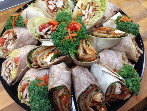 A platter of assorted wraps, including chicken and vegetables, garnished with kale and shredded carrots.