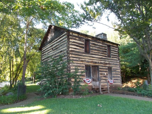 A rustic log cabin surrounded by trees, featuring a front porch and decorative bunting.