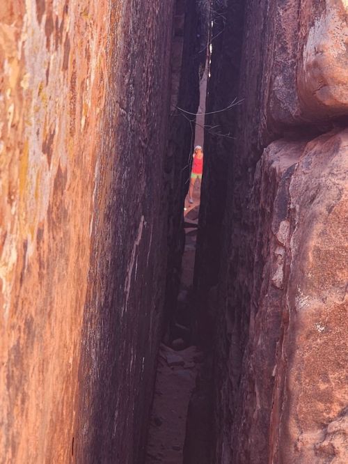 A narrow crevice between two large rock formations, with a person visible in the distance.