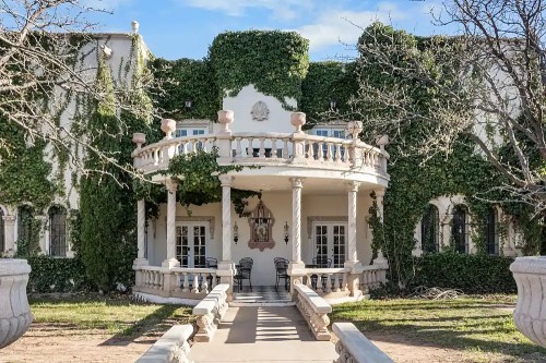 A grand, ivy-covered mansion with a circular balcony and stone pathway leading to the entrance.