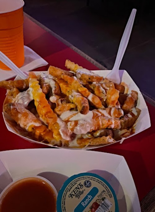 A serving of loaded fries topped with cheese and ranch sauce, served in a white tray with plastic utensils.
