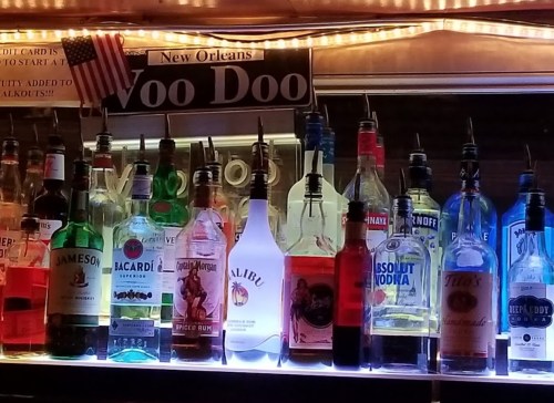 A colorful display of various liquor bottles on a bar shelf, illuminated by soft lights.