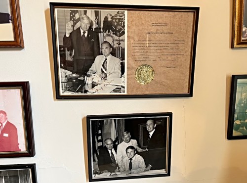 Two framed photographs on a wall: one of a man swearing in another, and another of a group of men at a table.