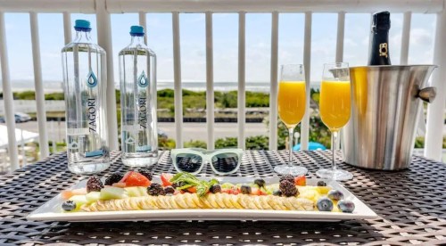 A platter of fresh fruit and crackers, two glasses of orange juice, and water bottles on a balcony table.