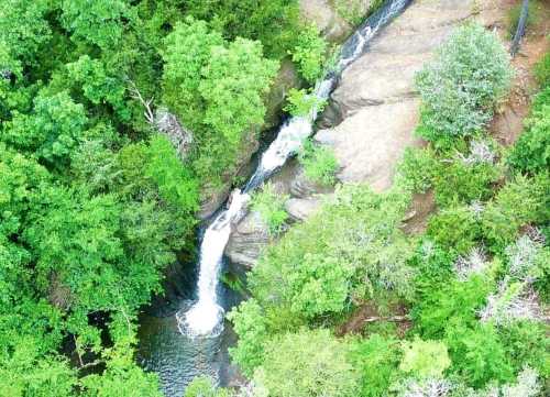 Aerial view of a waterfall cascading over rocks, surrounded by lush green trees and foliage.