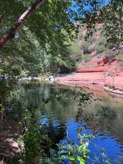 A serene river surrounded by lush greenery and red rock formations under a clear blue sky.