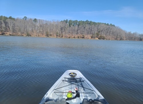 A kayak on calm water, with trees lining the shore under a clear blue sky.