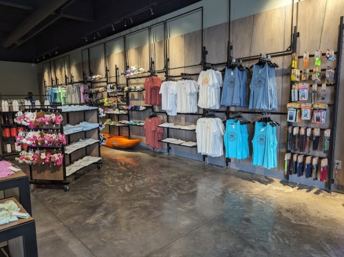A retail store interior featuring shelves of clothing, accessories, and a kayak on display.