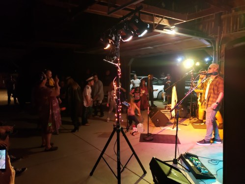 A live band performs in a dimly lit garage, with an audience enjoying the music and dancing.