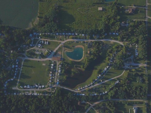 Aerial view of a campground with tents, RVs, and a small pond surrounded by greenery.