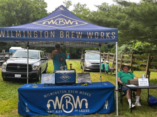 A vendor booth for Wilmington Brew Works with a man serving drinks and another man sitting at a table.