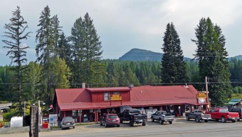 A red-roofed building surrounded by tall trees and mountains, with parked cars in front on a cloudy day.