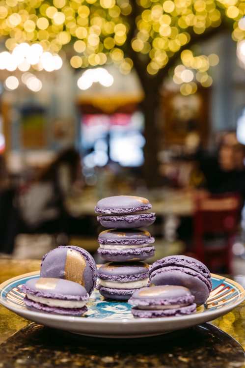 A plate of purple macarons stacked, with a blurred background of warm, glowing lights.