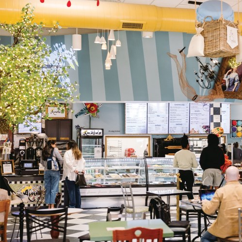 A cozy café interior with a display case, colorful decor, and customers ordering at the counter.