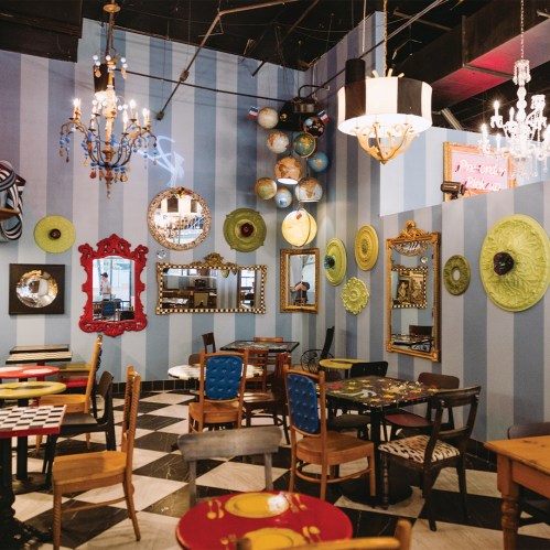 Colorful café interior with striped walls, eclectic mirrors, chandeliers, and unique tables and chairs.