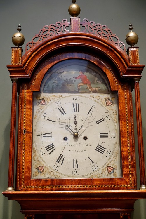 Antique wooden clock with ornate design, featuring a painted scene and Roman numerals on the clock face.