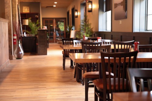 Interior of a restaurant featuring wooden tables and chairs, with a warm, inviting atmosphere and natural lighting.