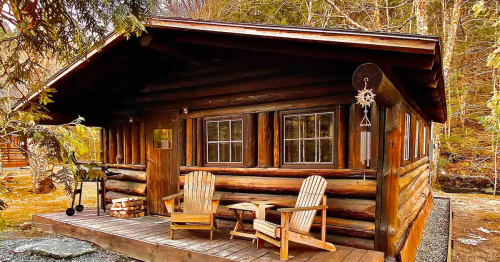 A cozy log cabin with two wooden chairs on the porch, surrounded by trees and nature.