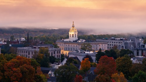 A scenic view of a historic building with a golden dome, surrounded by autumn foliage and misty mountains at sunset.
