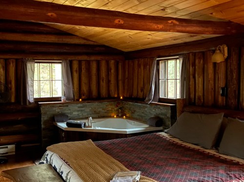 Cozy log cabin interior with a bed, a bathtub, and windows letting in natural light. Warm, rustic decor.