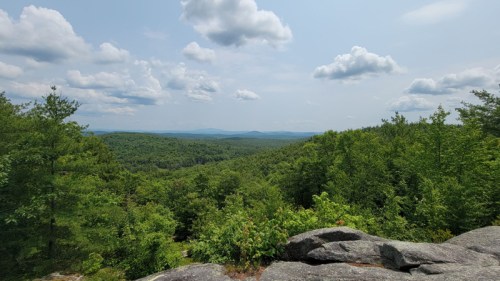 A panoramic view of lush green forests and rolling hills under a partly cloudy sky.