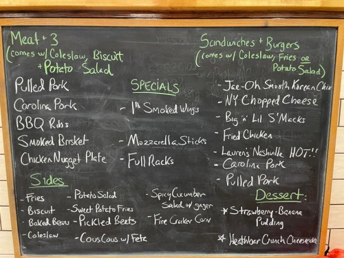 Chalkboard menu featuring pulled pork, BBQ ribs, sides, sandwiches, burgers, and desserts like strawberry banana pudding.