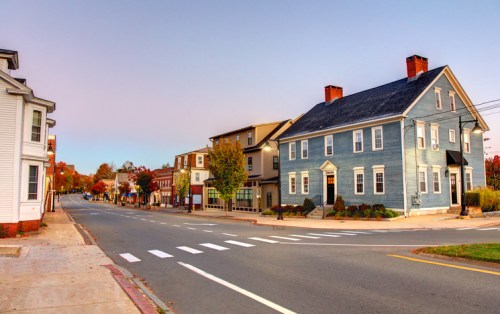 A quiet street scene featuring a blue house, trees, and charming buildings under a clear sky during autumn.
