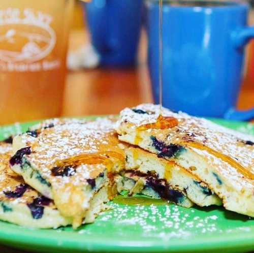 Fluffy blueberry pancakes drizzled with syrup, dusted with powdered sugar, served on a green plate.