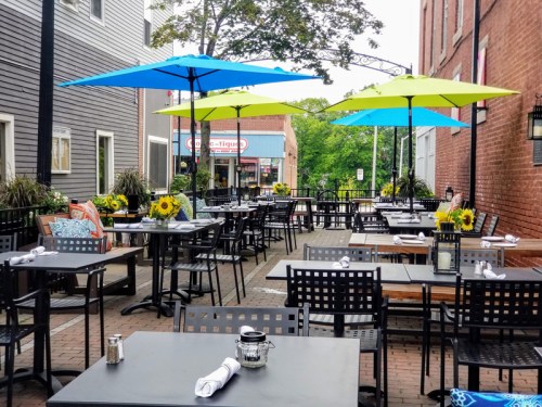 Outdoor restaurant patio with black tables, colorful umbrellas, and sunflowers, set in a charming urban area.