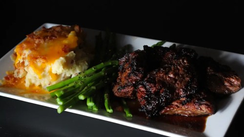 A plate featuring grilled steak, green asparagus, and cheesy mashed potatoes.